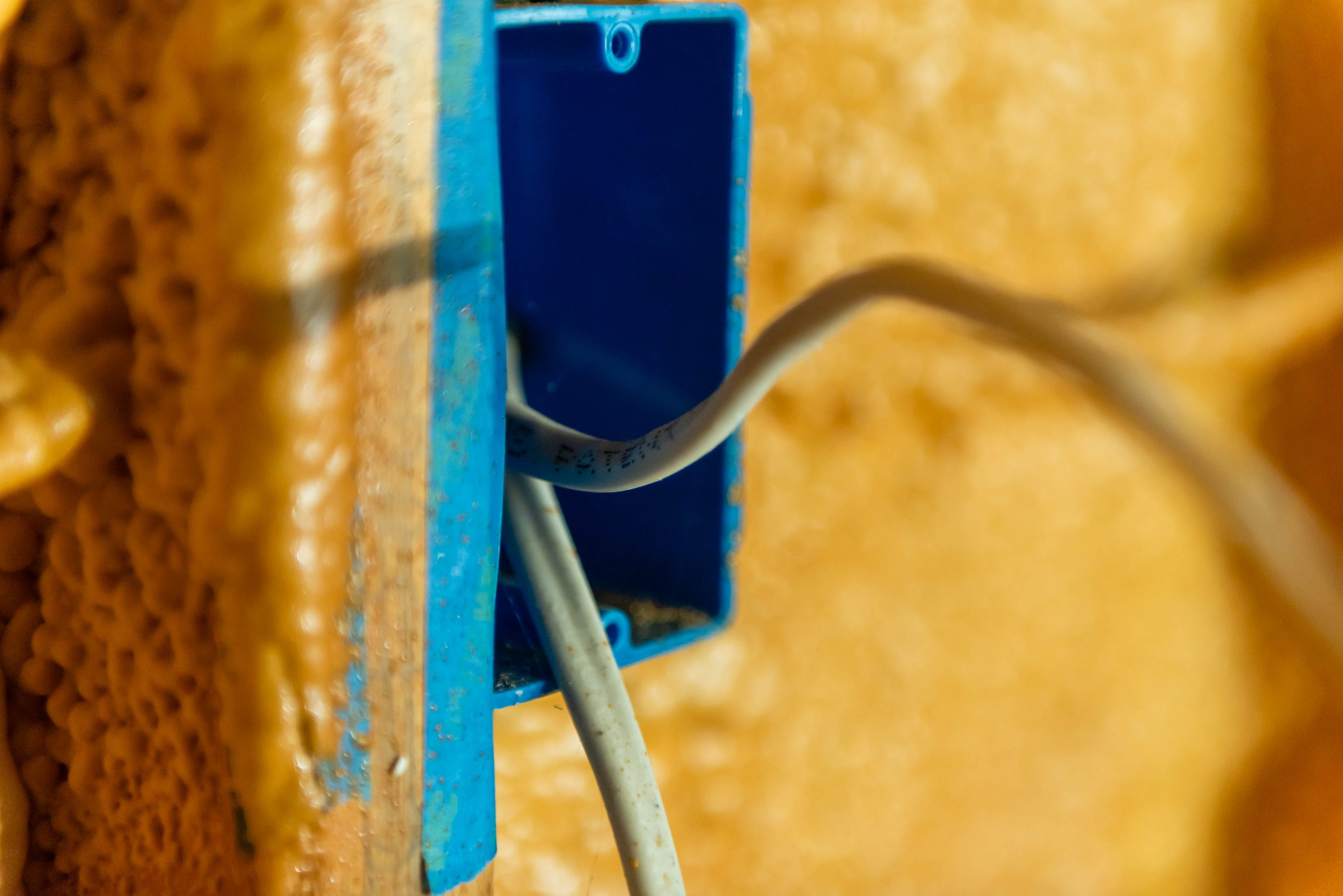 Romex wire running into blue outlet box surrounded by spray foam — Casta Energy installation close-up