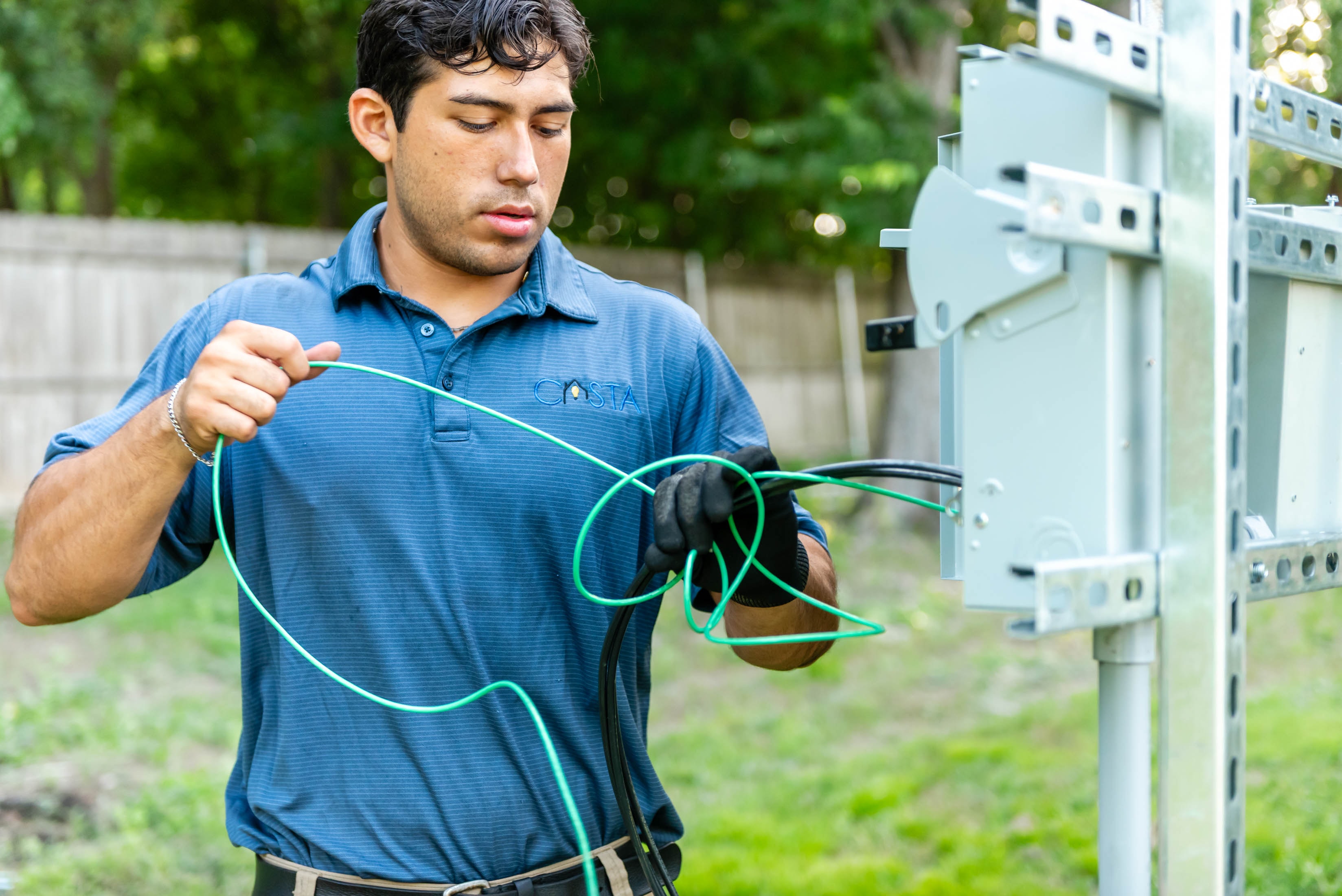 Casta Energy technician in branded polo managing green ground wire at outdoor solar panel disconnect