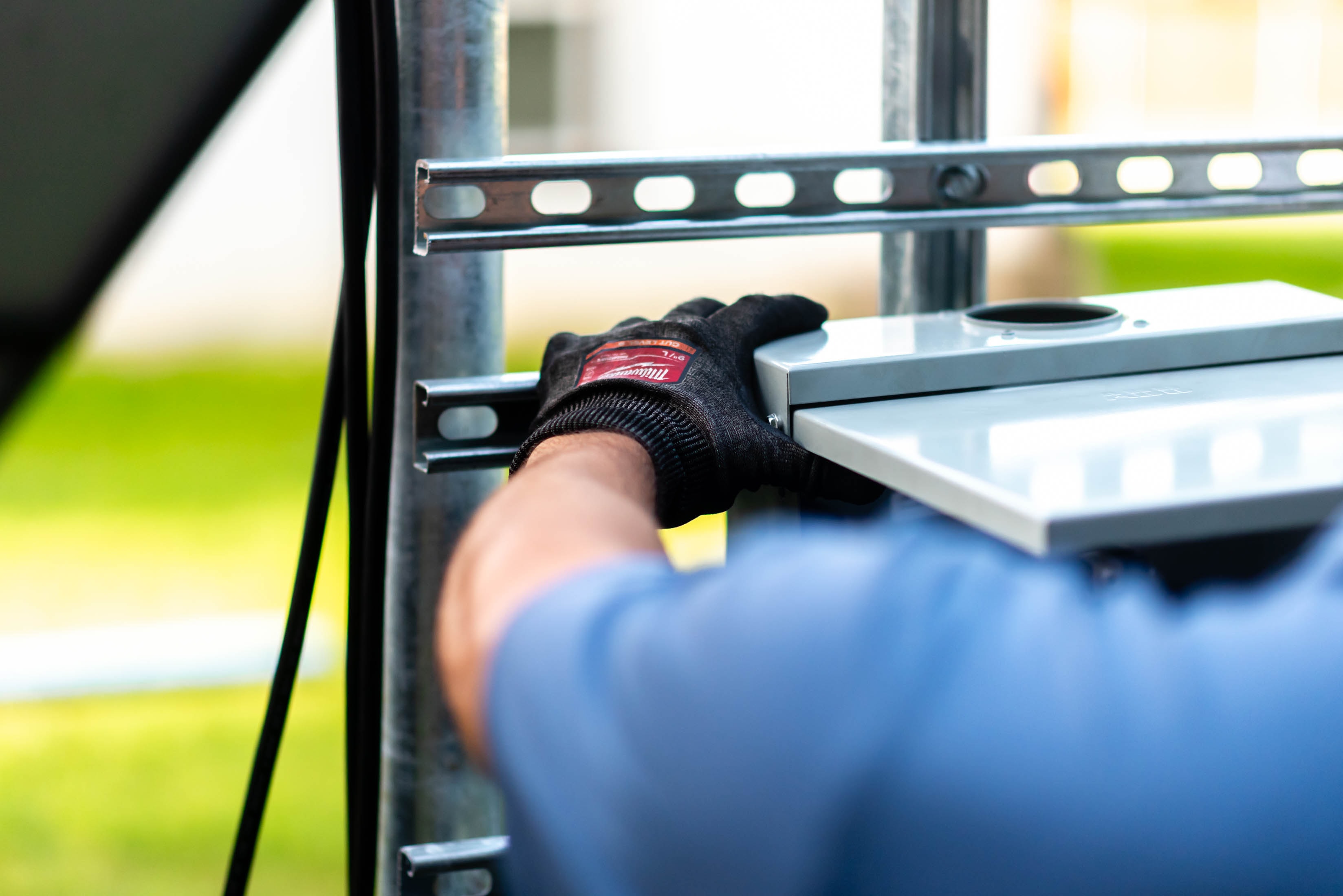 Gloved hand positioning disconnect enclosure onto solar racking strut — Casta Energy install detail