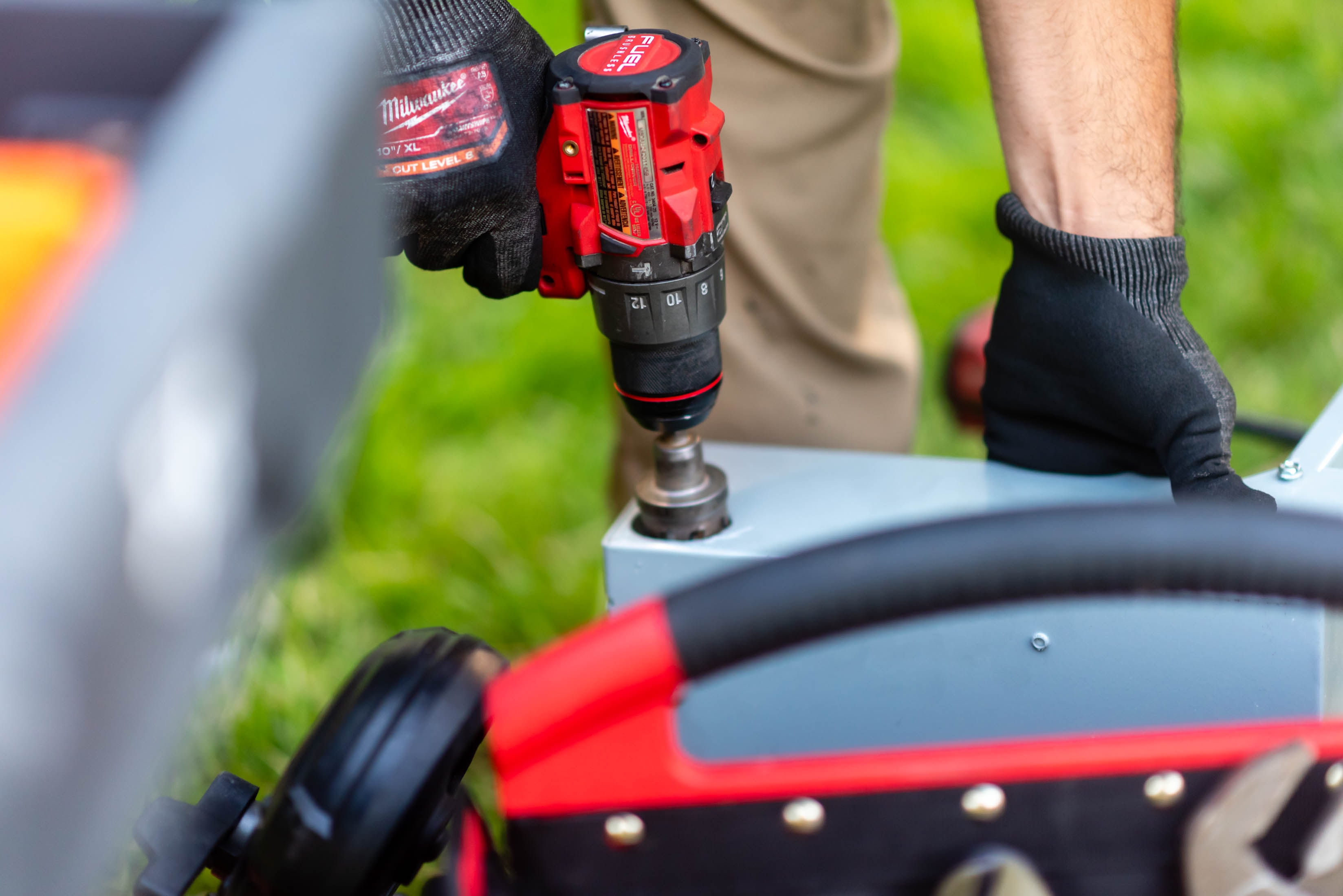 Close-up of Milwaukee FUEL drill held in gloved hands drilling into disconnect box — Casta Energy