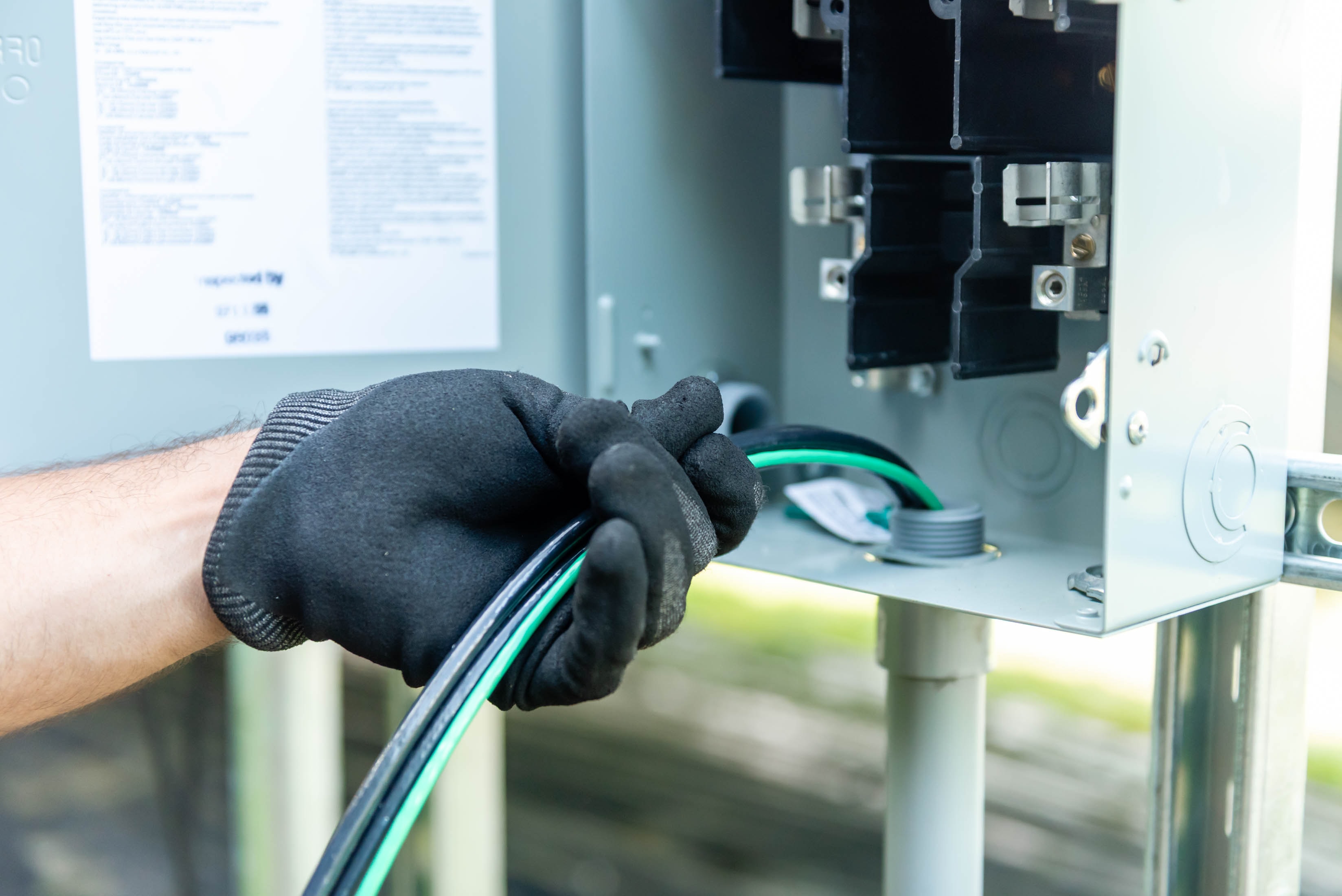 Gloved hands pulling black and green wire into outdoor disconnect panel — Casta Energy solar install