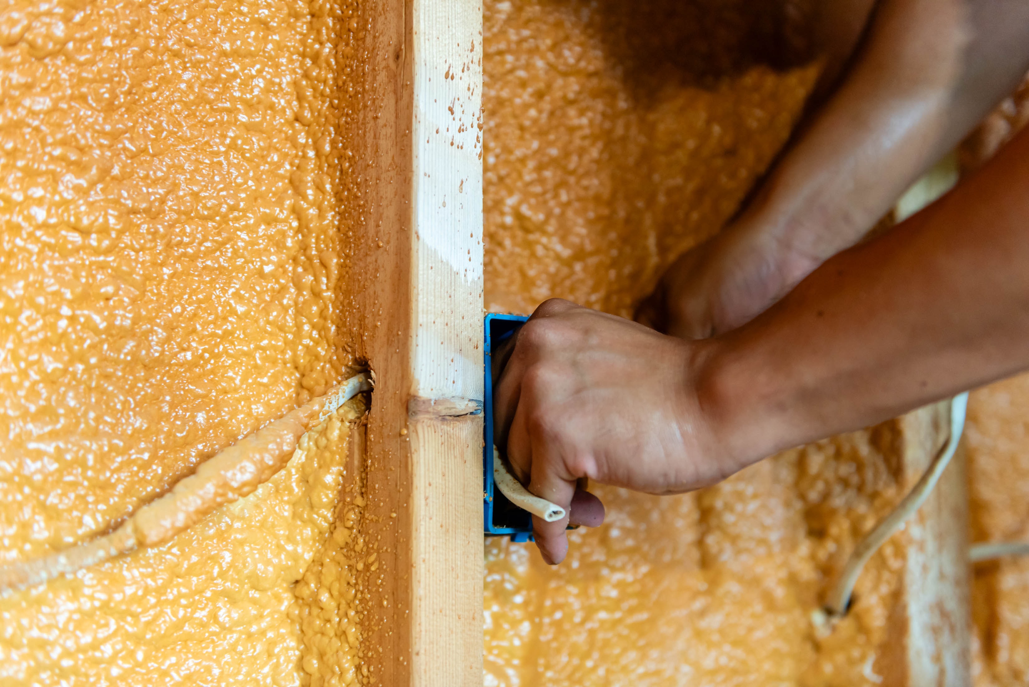 Close-up of hand positioning blue outlet box in spray foam wall — Casta Energy new construction wiring