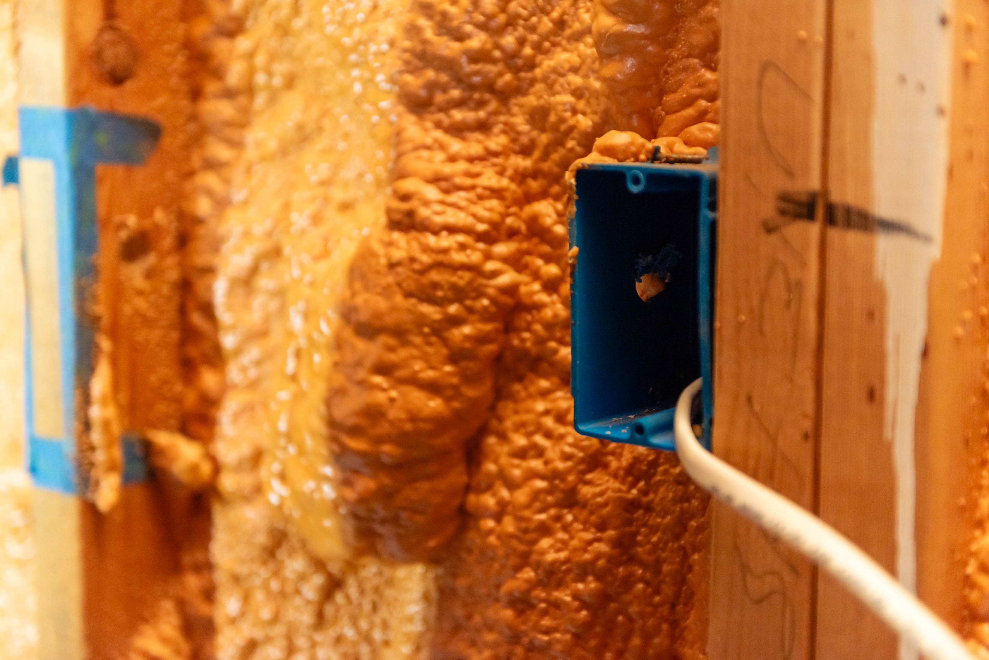 Blue electrical outlet box set in spray foam insulation with Romex wire — Casta Energy rough-in detail
