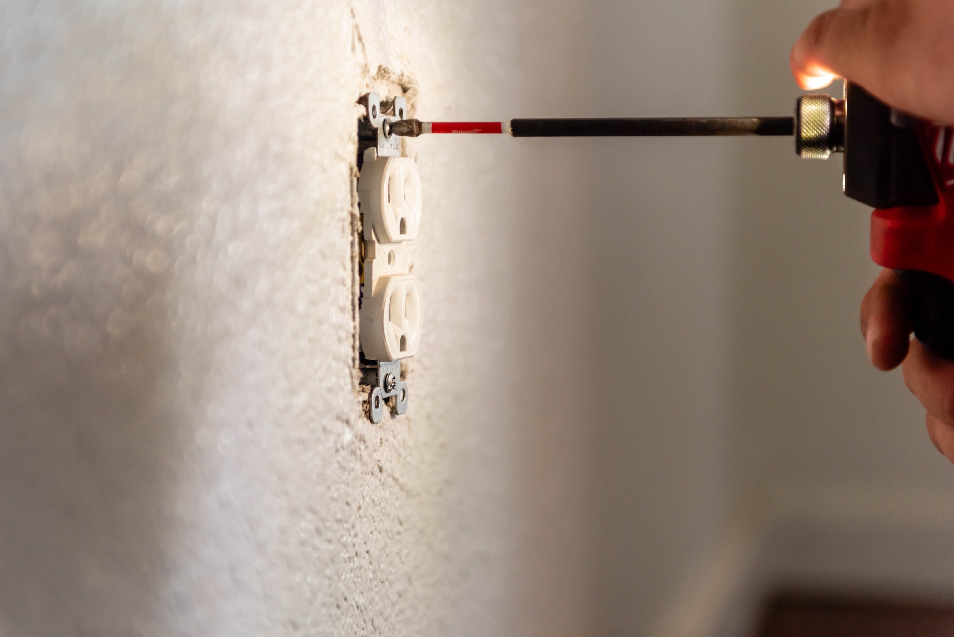 Close-up of hand tightening duplex outlet into stucco wall with Milwaukee screwdriver — Casta Energy