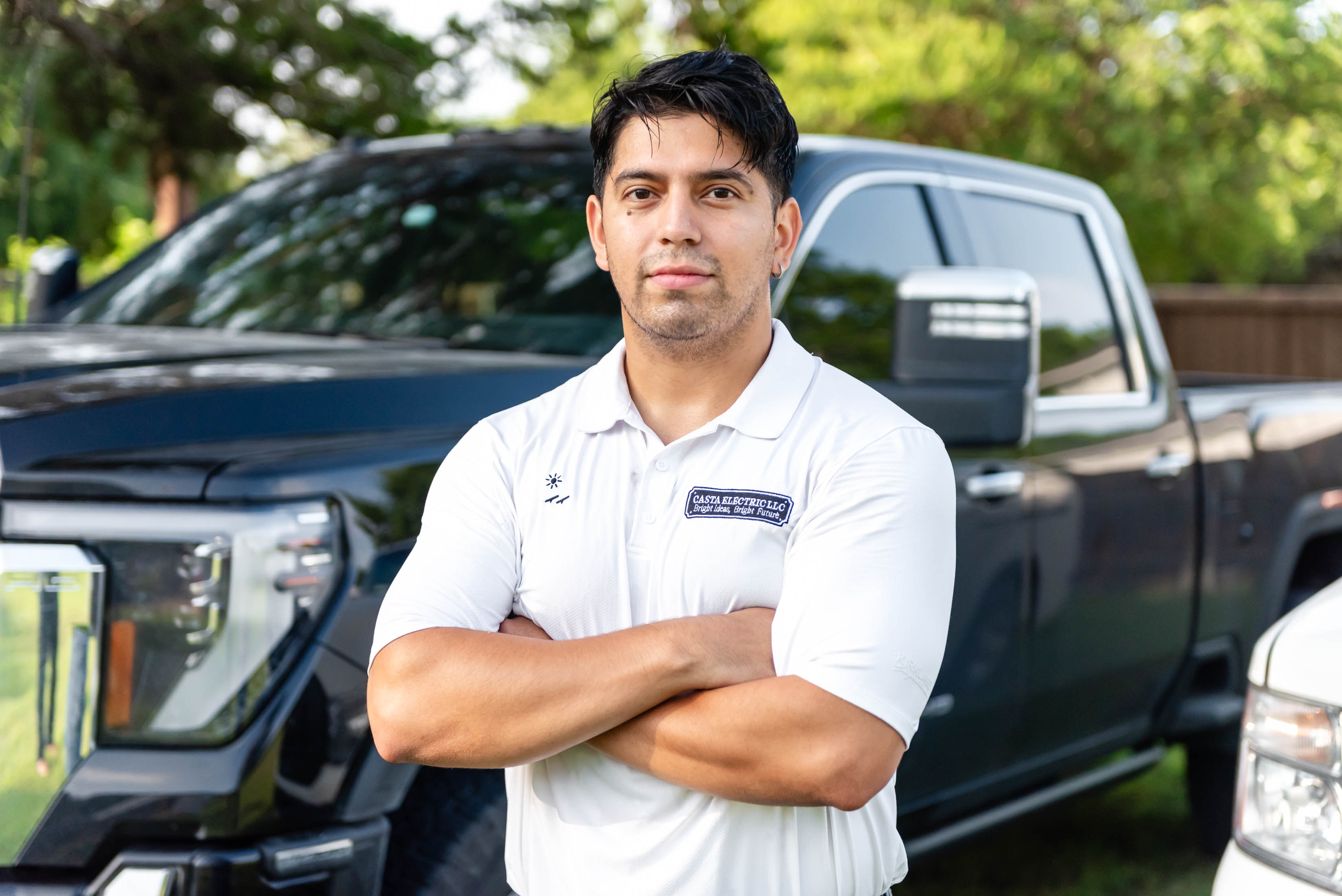 Casta Electric LLC owner in white polo standing arms crossed in front of GMC truck