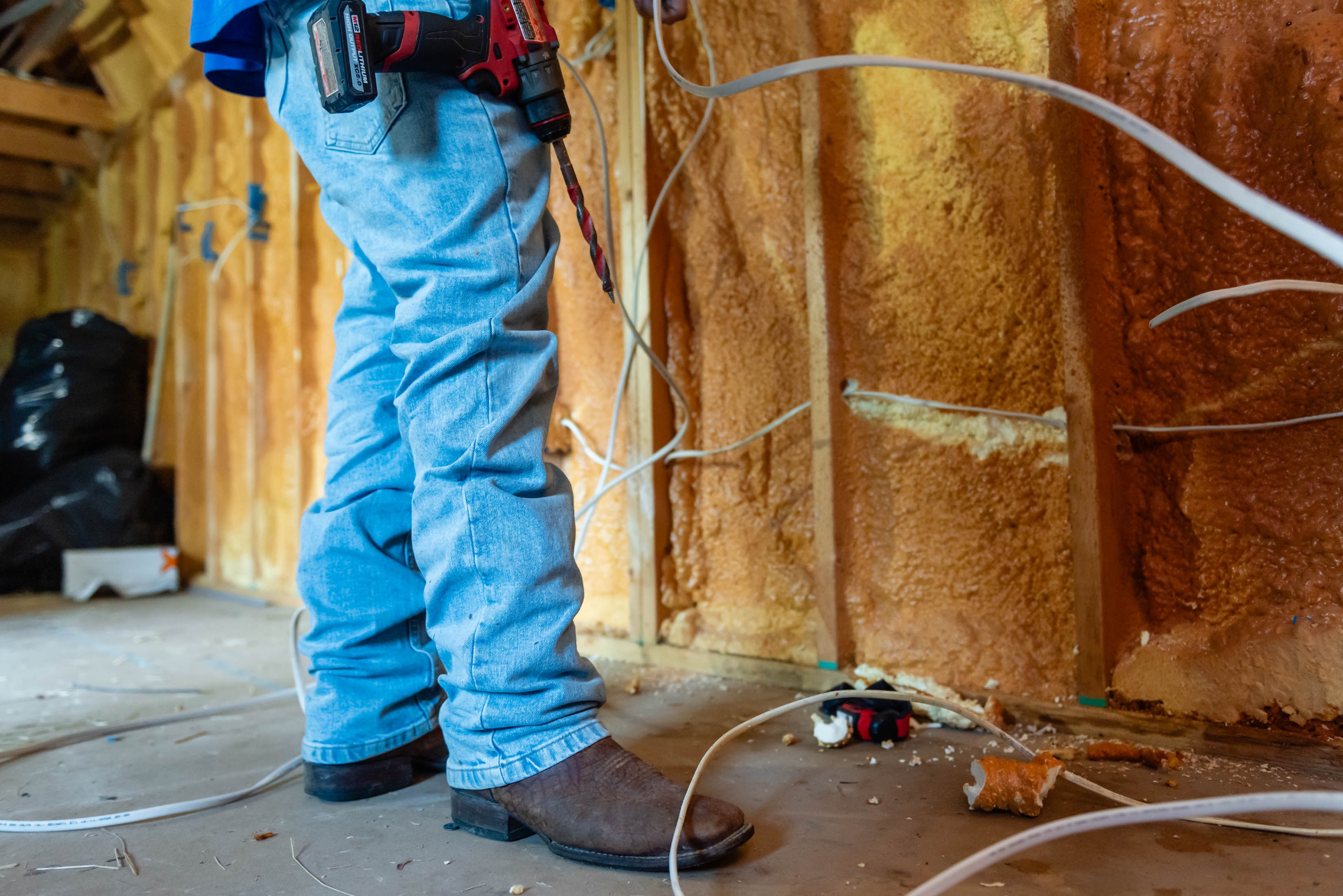Casta Energy tech in cowboy boots holding Milwaukee drill on spray foam job site
