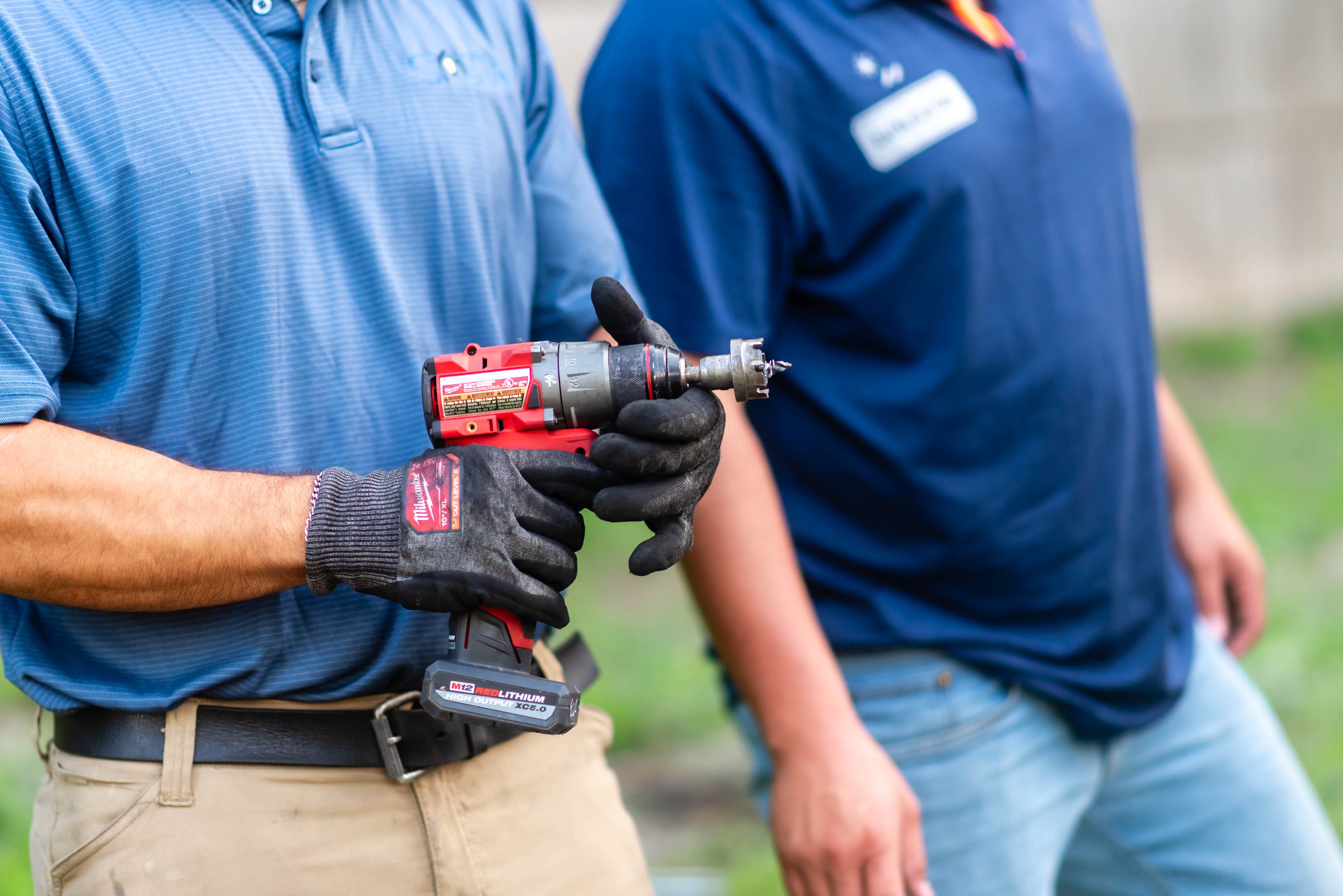 Casta Energy tech in blue polo holding Milwaukee M12 drill with hole saw bit — solar disconnect install