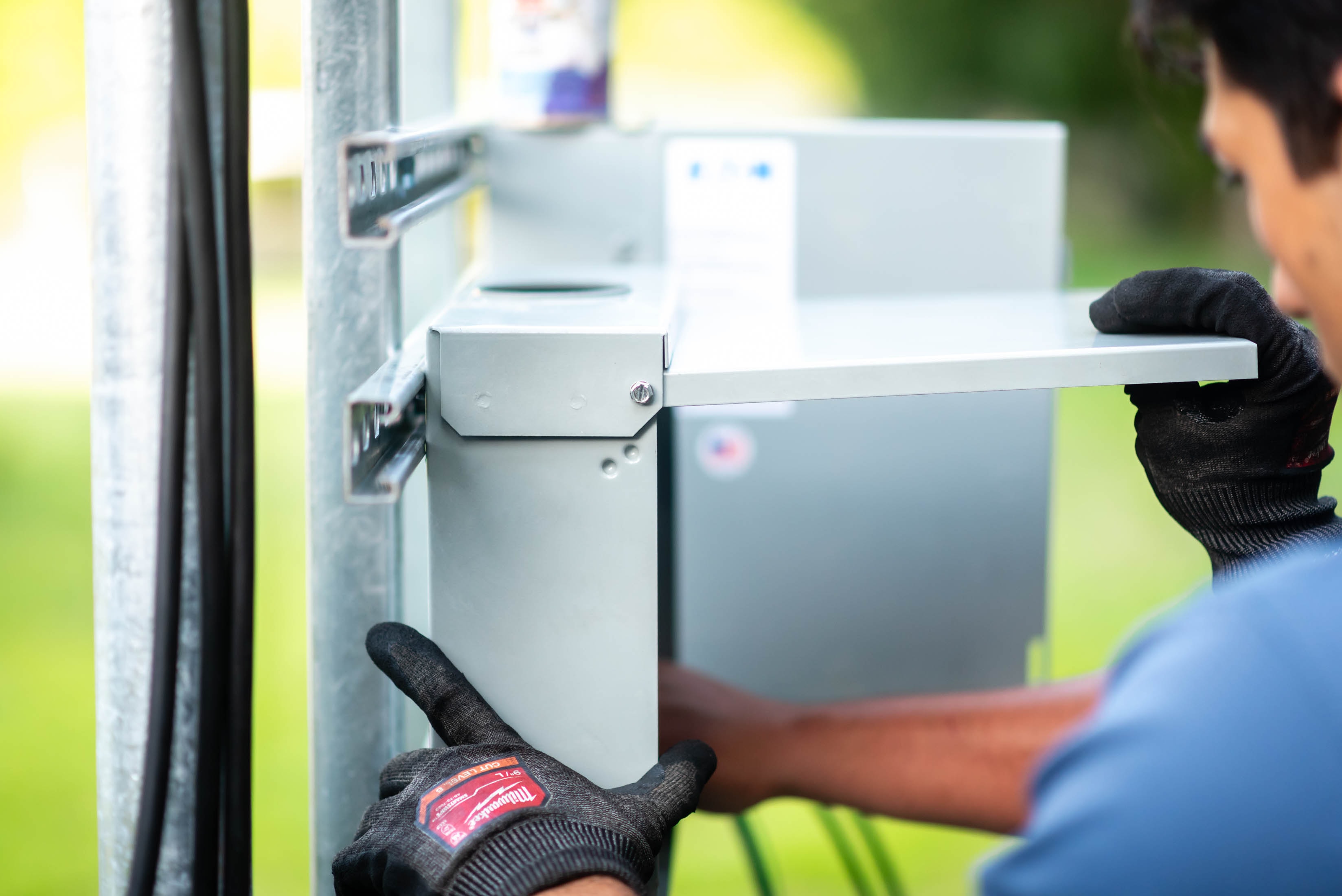 Casta Energy tech in blue polo mounting disconnect box onto unistrut solar racking with Milwaukee gloves