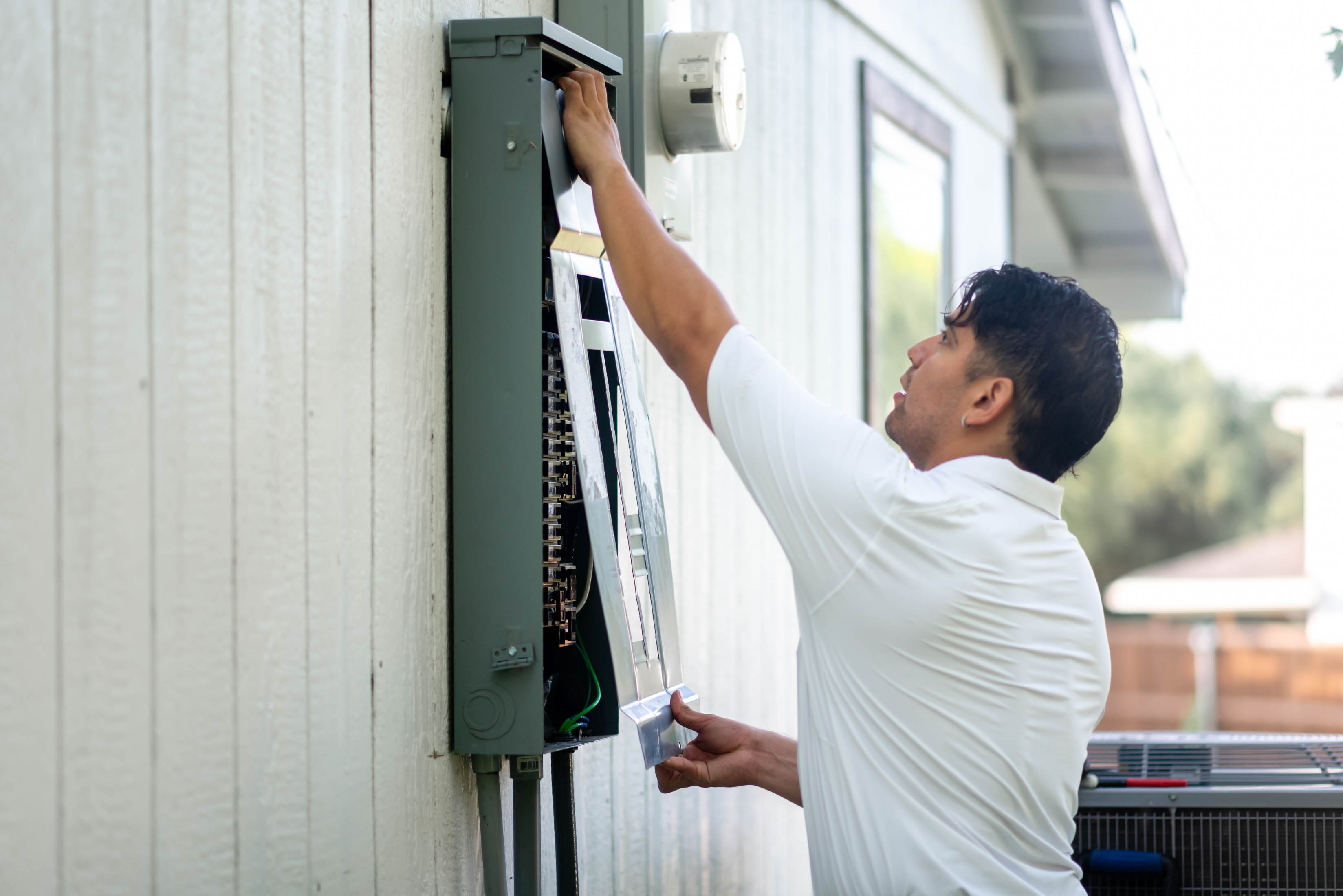 Casta Energy tech reaching into open outdoor main panel on side of house — panel upgrade service
