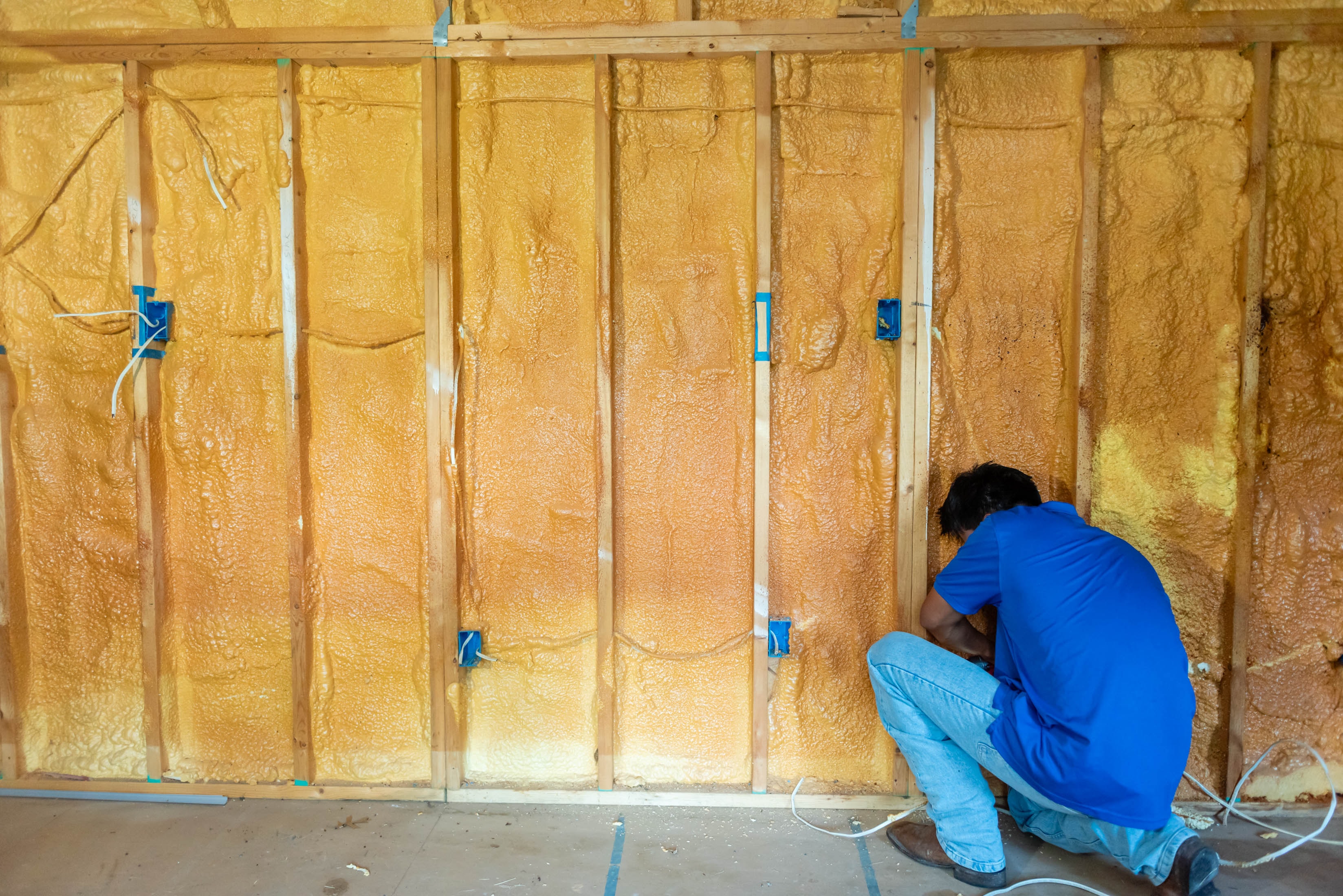 Casta Energy tech crouching at spray foam insulated wall with blue outlet boxes — new construction rough-in