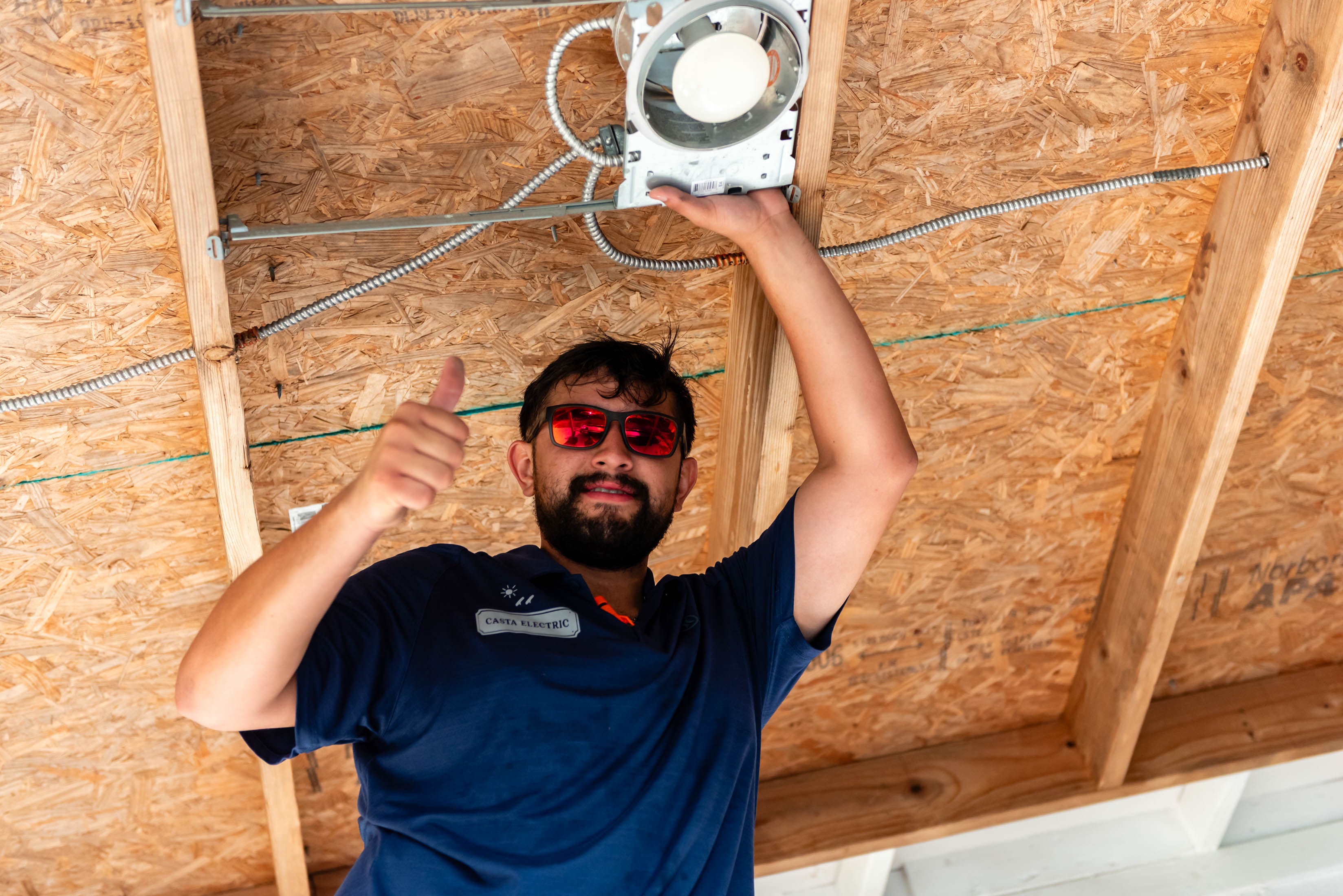 Casta Electric tech giving thumbs up while installing ceiling light — job done right