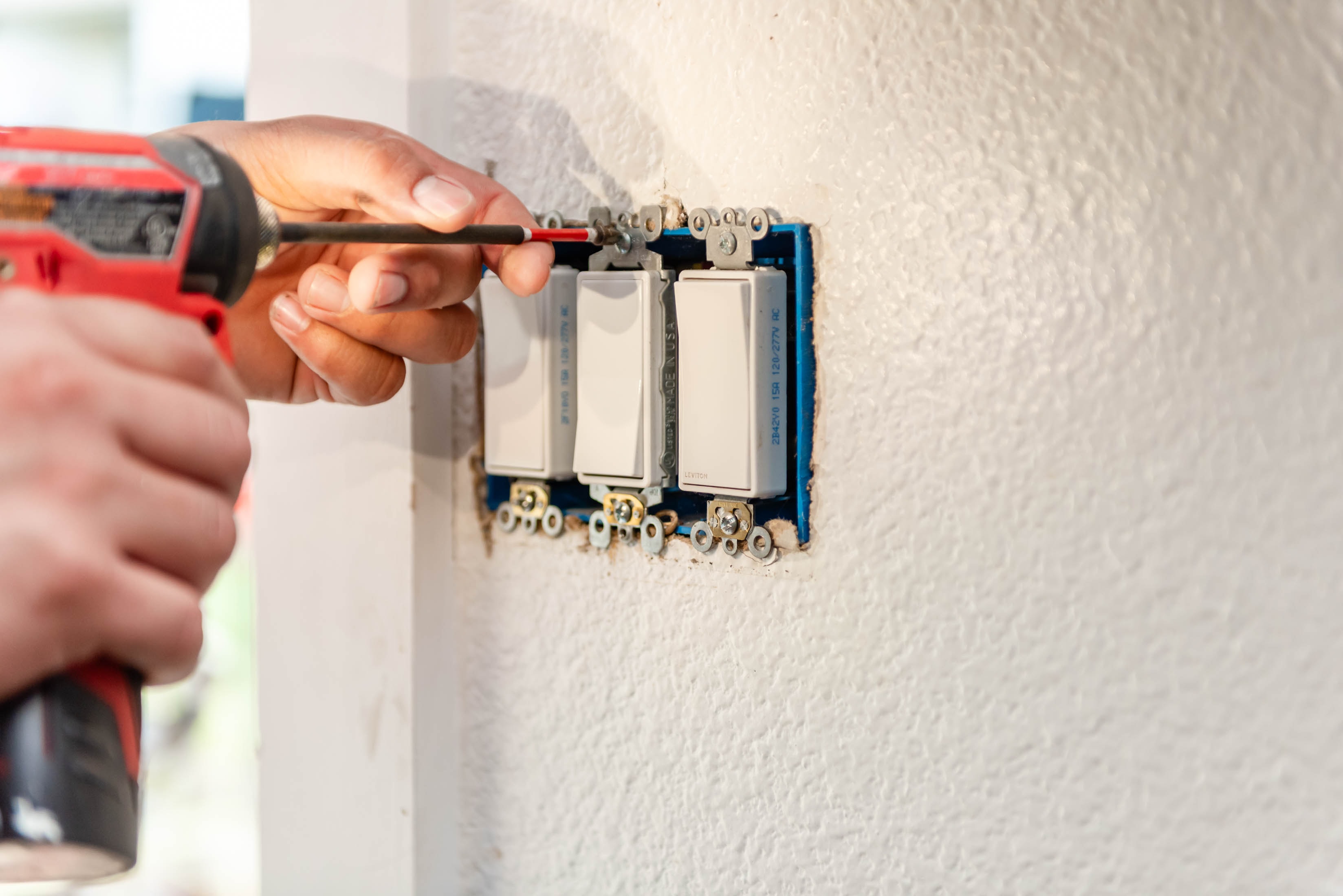 Milwaukee drill securing triple Leviton rocker switch gang box into stucco wall — Casta Energy